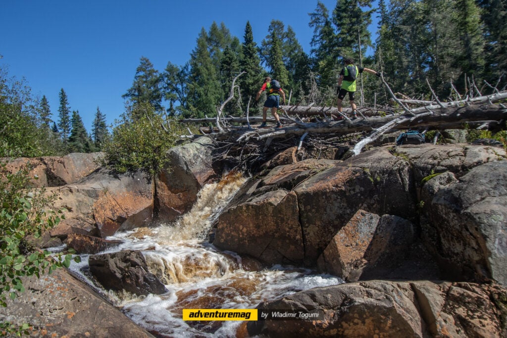 Sur des caps rocheux où s'écoule une cascade, des athlètes du Raid Témiscamingue traversent le parcours rocailleux. 